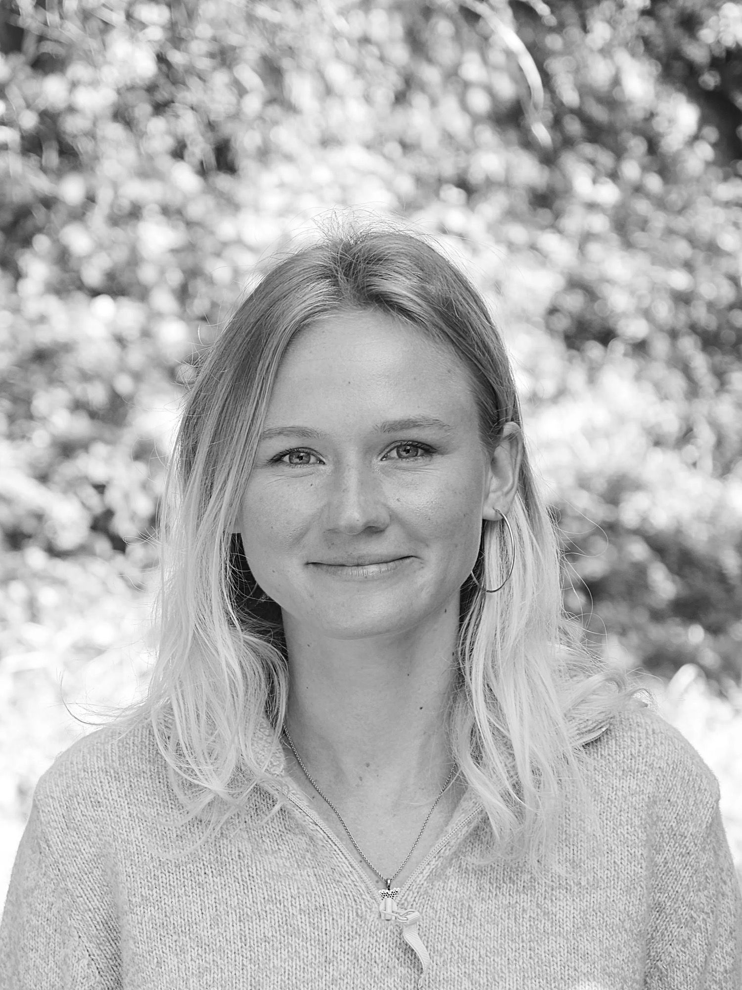 Portrait en noir et blanc d’Alizé Foveau, souriante, devant un feuillage.