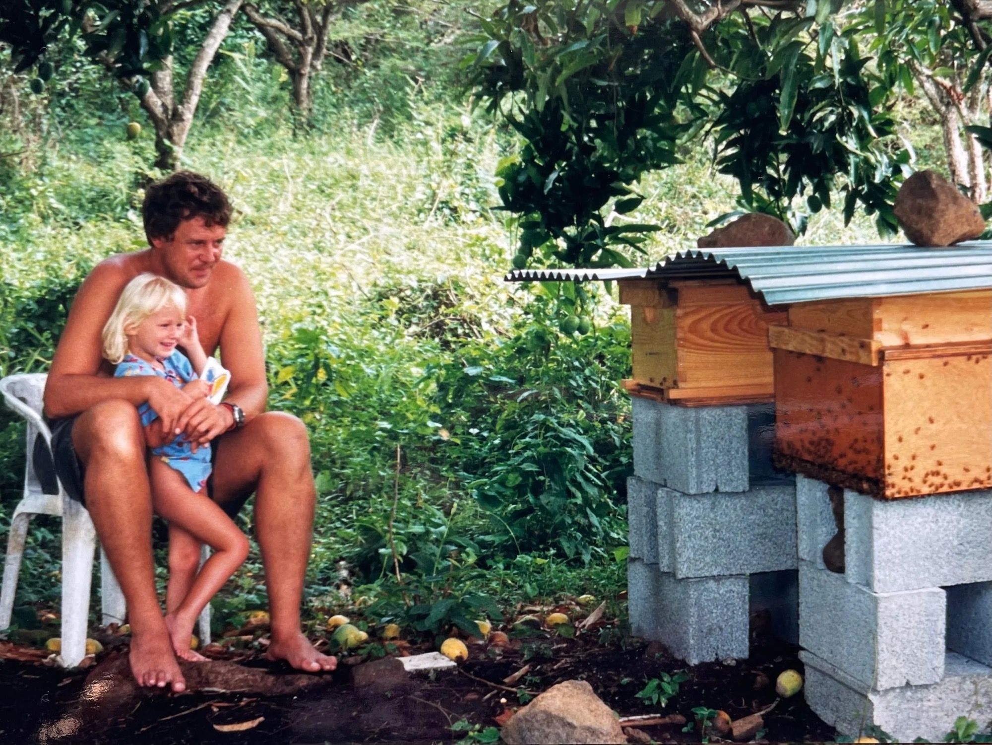 Alizé enfant, sur les genoux de son père, devant les ruches.