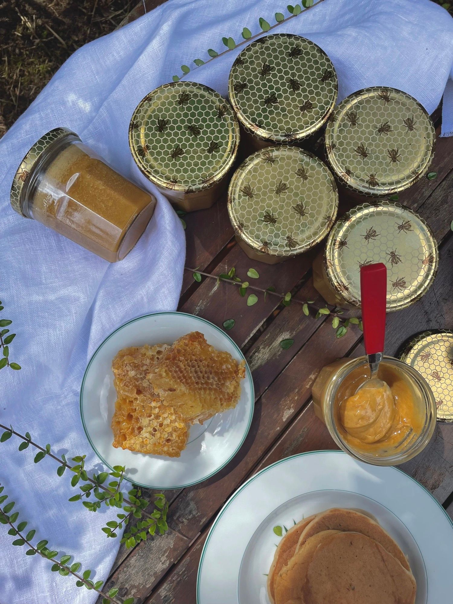 Des pots de miel à couvercles nid-d’abeille et un rayon de cire, posés sur un drap blanc.