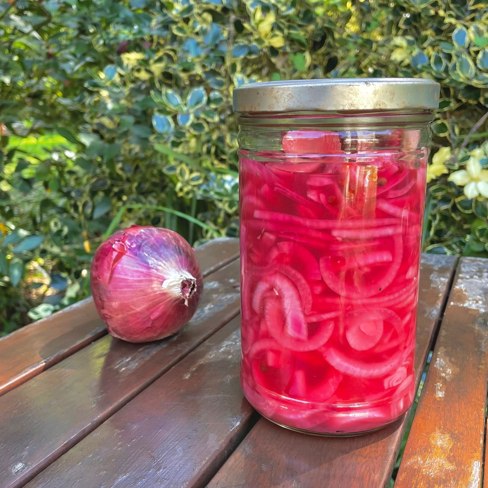 Un bocal d’oignons rouges au vinaigre, d’un rose vif, à côté d’un oignon entier.