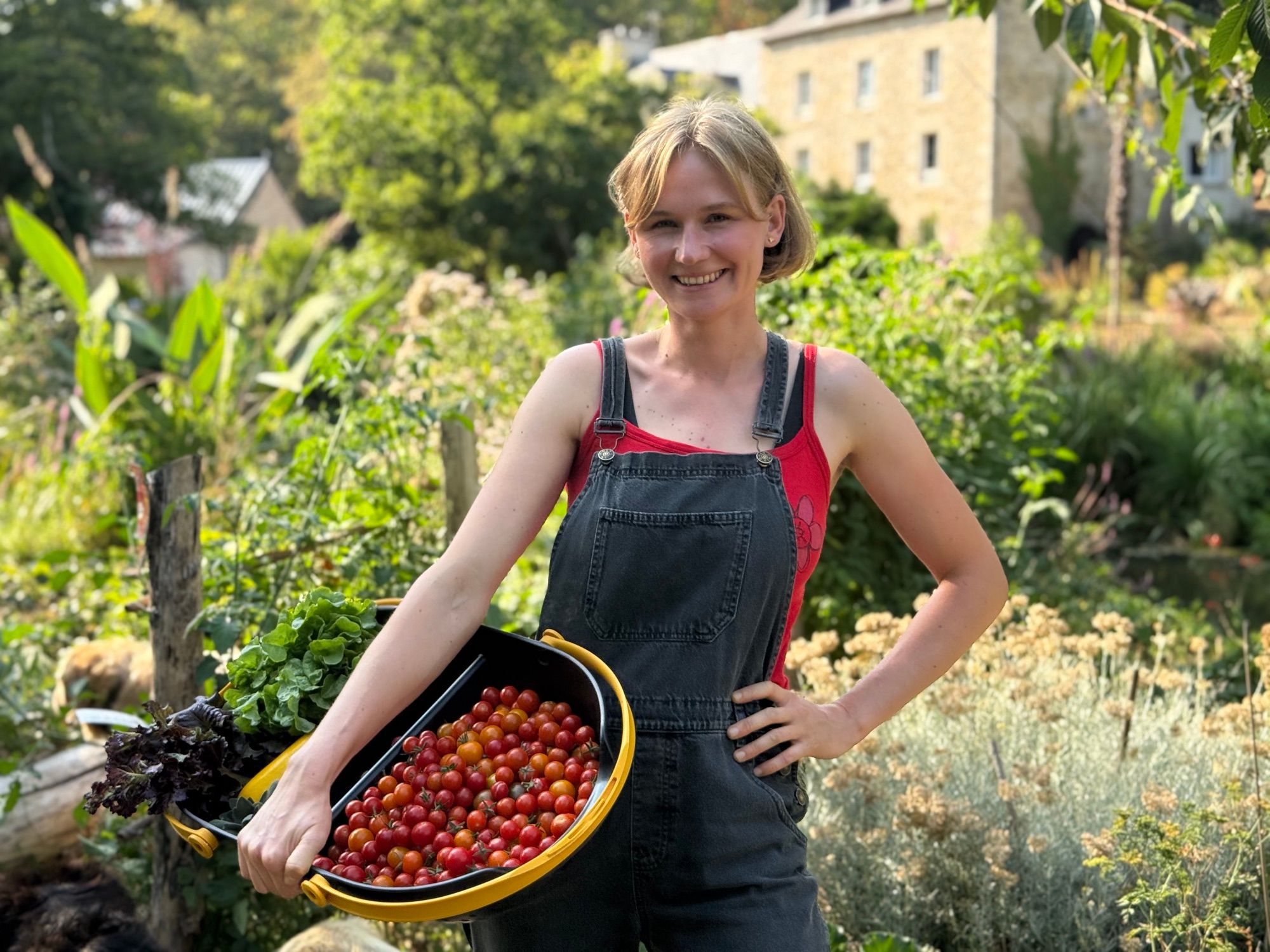 Alizé Foveau devant le moulin, un bac de tomates cerises et de salades au bras.