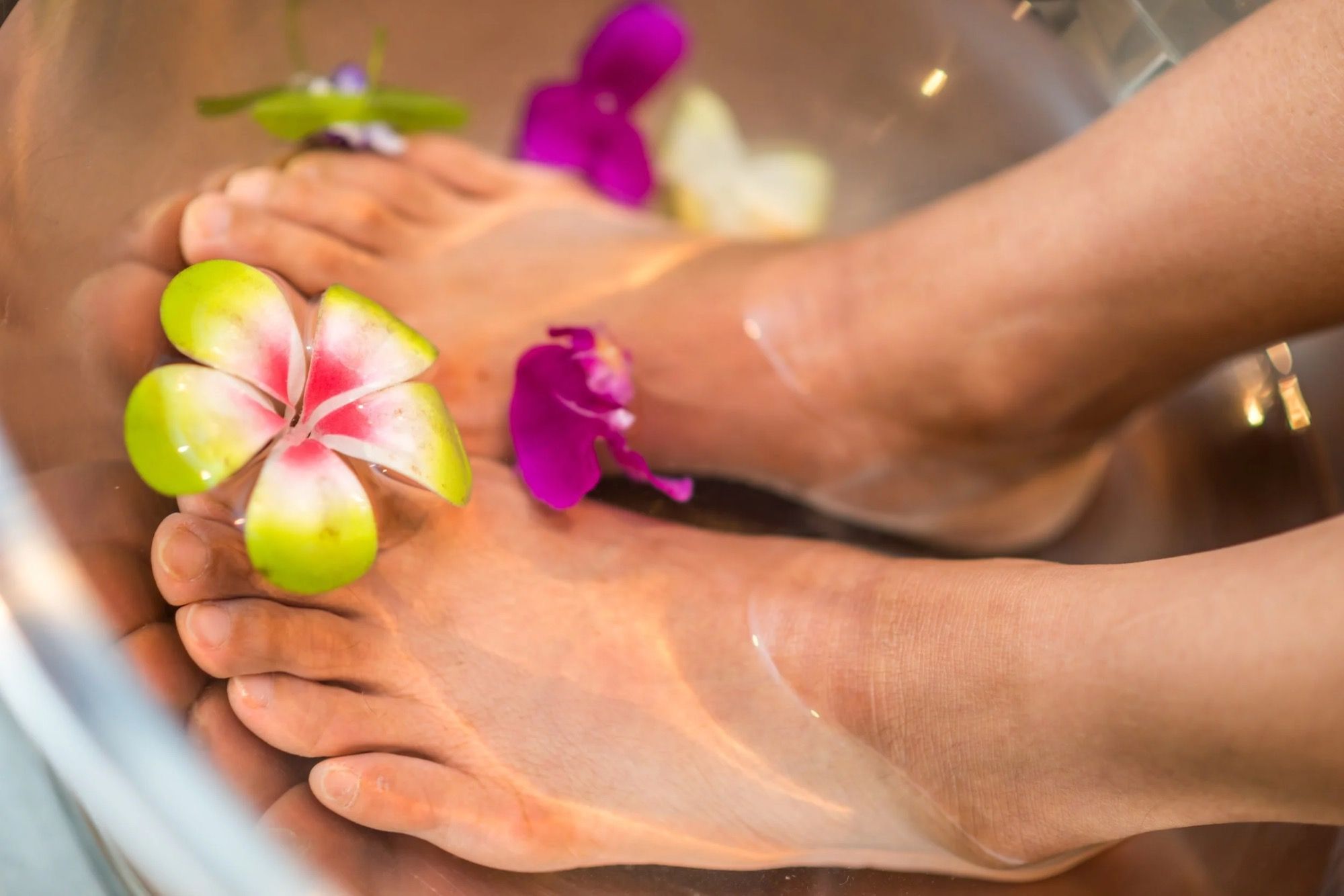 Deux pieds dans un bain d’eau tiède où flottent des fleurs, avant un soin.