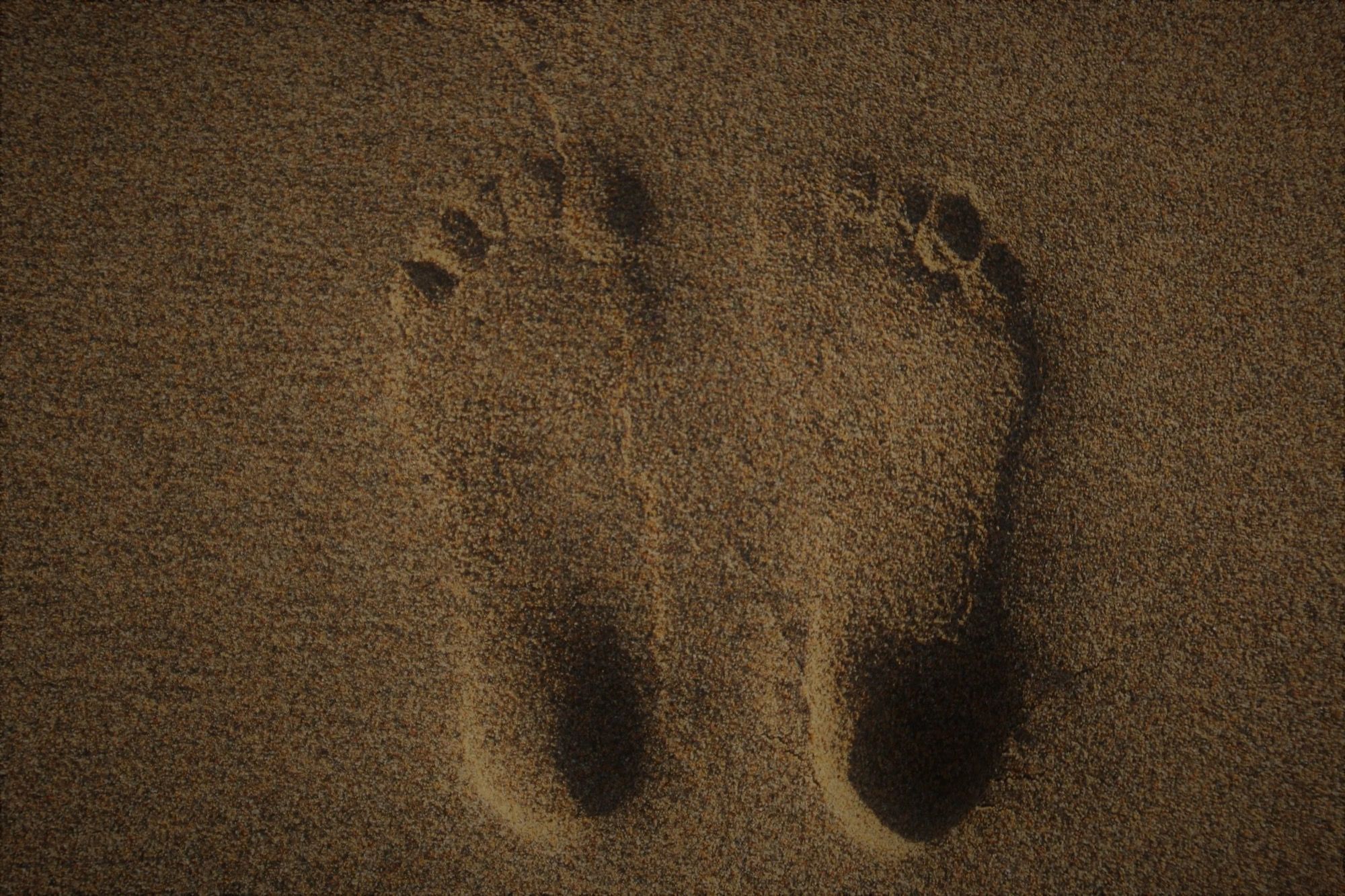 Deux empreintes de pieds nus laissées dans le sable d’une plage.