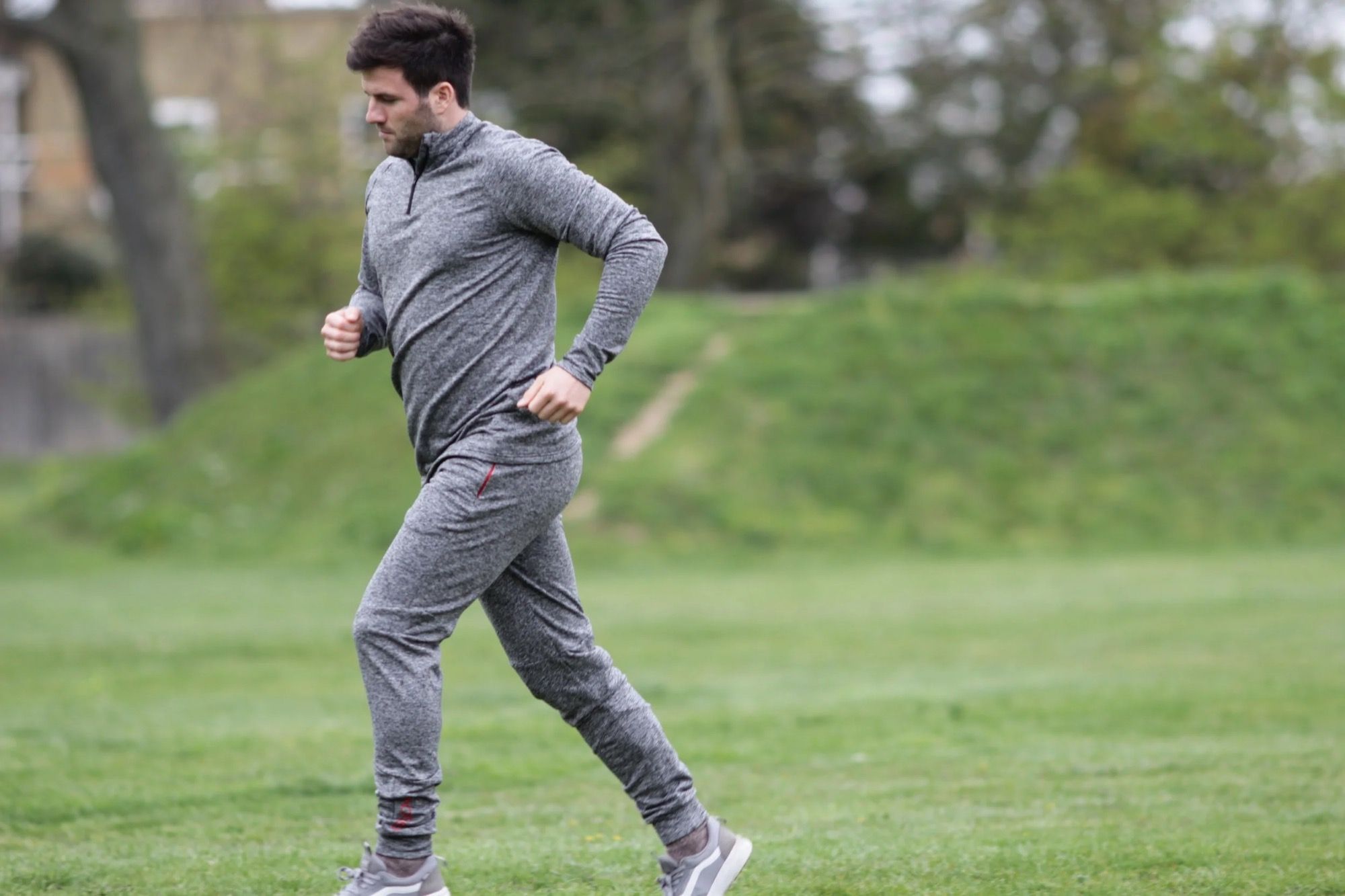 Un coureur en survêtement s’entraîne dehors, sur l’herbe.